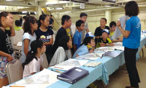 施設で地図を広げて係員の説明を聞く子ども達の学習風景